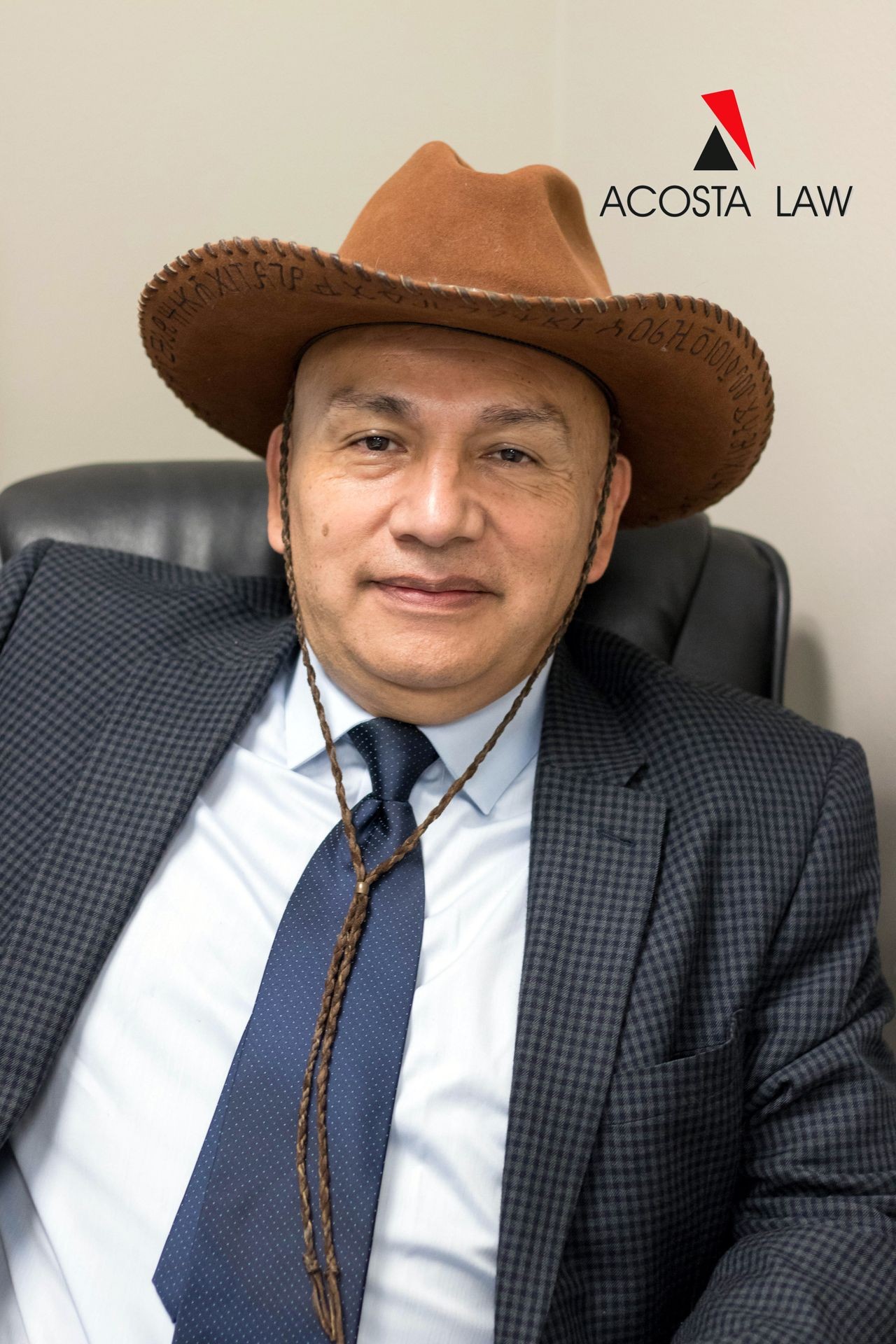 Man in cowboy hat and suit sitting in office chair with Acosta Law logo in background.