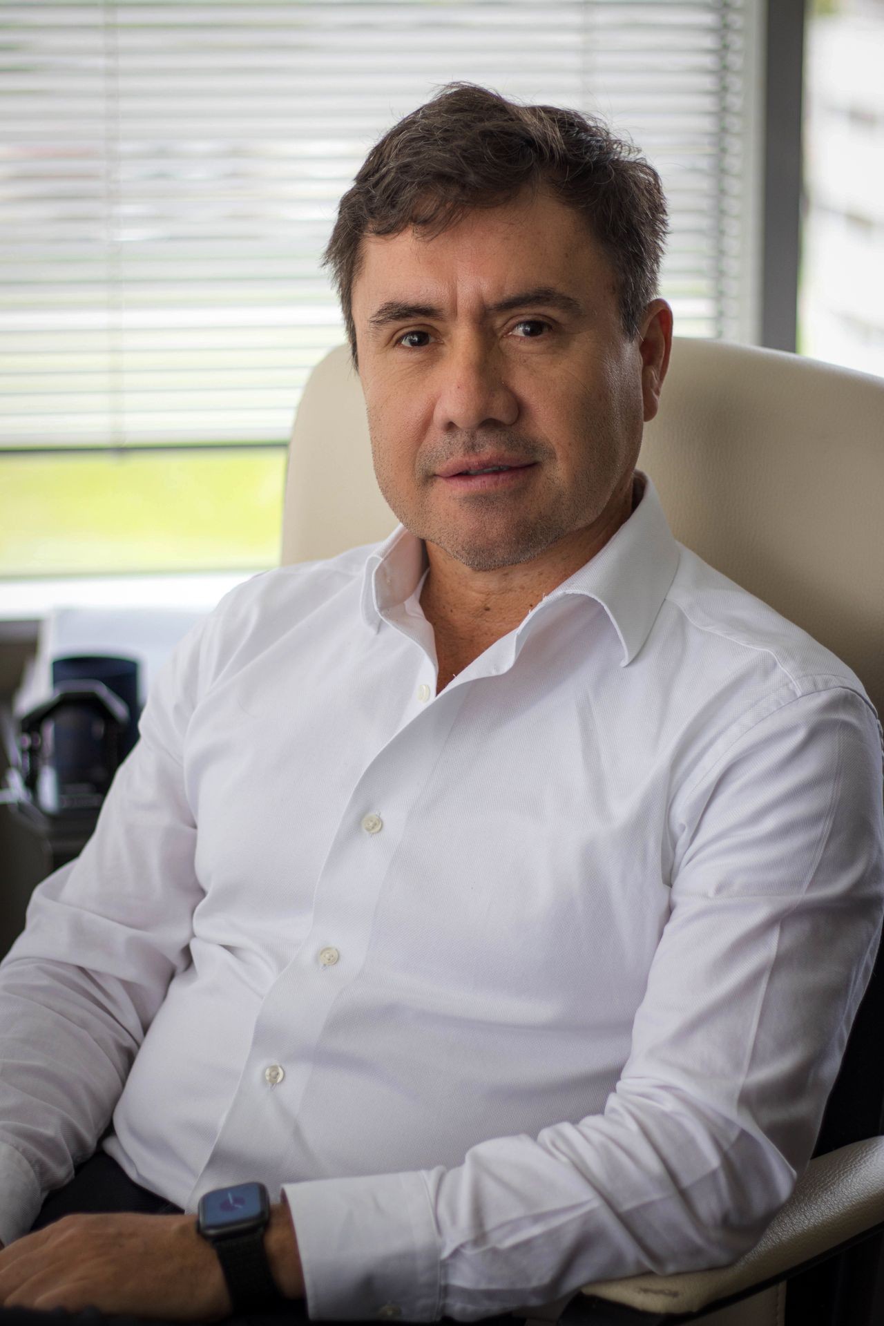 Person in a white dress shirt sitting in an office chair with window blinds in the background.